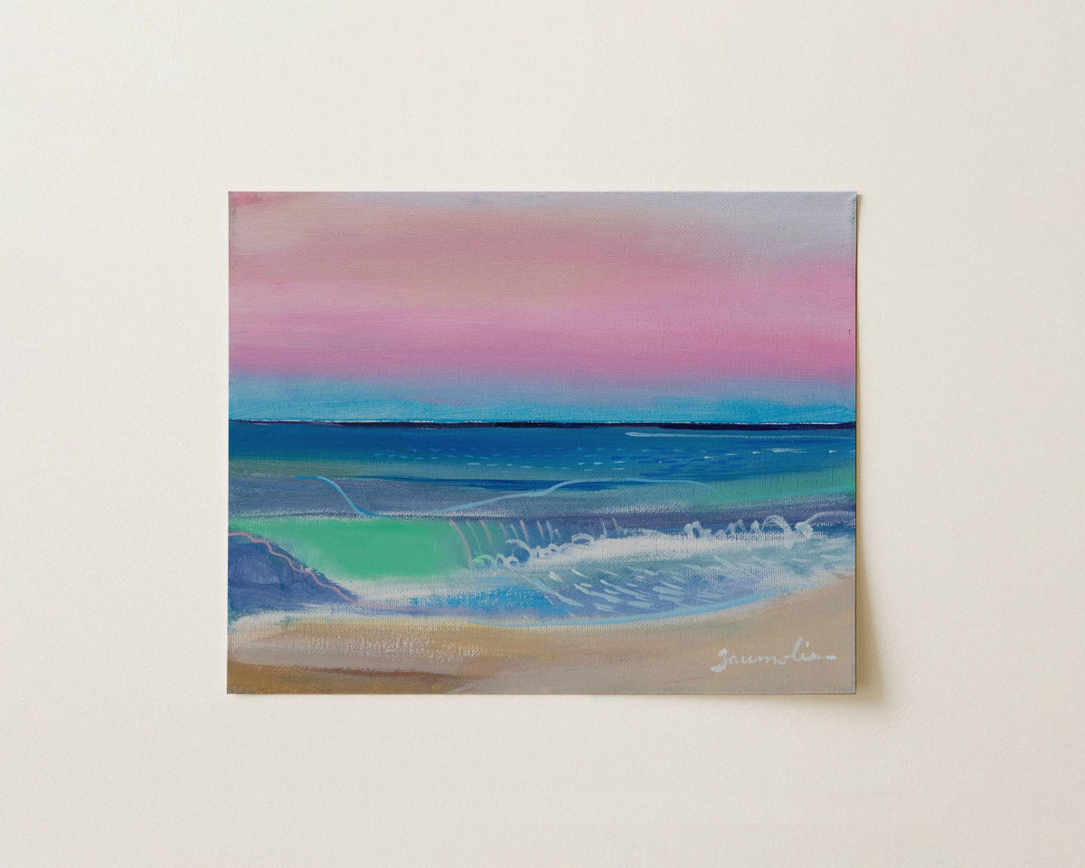 An abstract pastel painting of a beach scene with pink and blue sky, turquoise water, white surf, and sandy shore, displayed against a light beige wall.