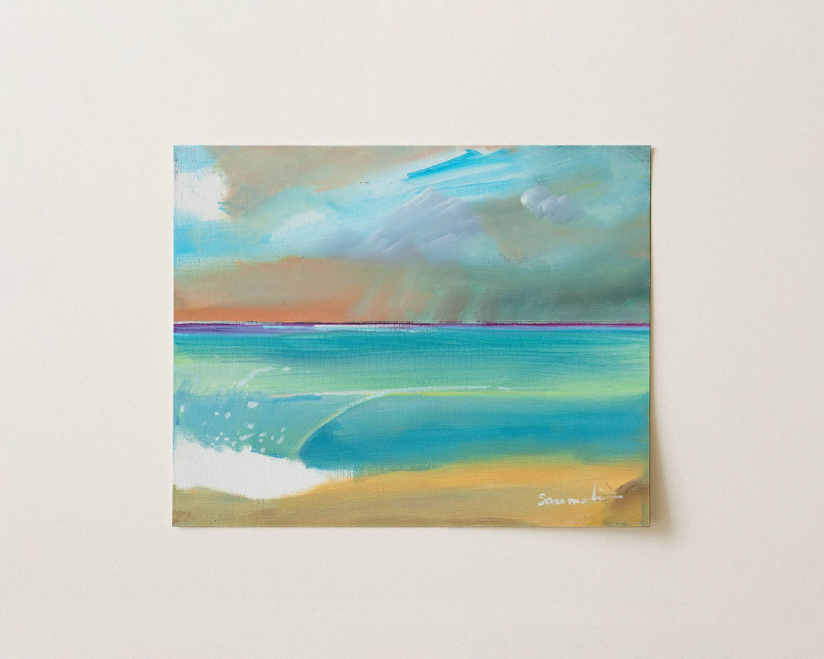An abstract landscape painting of a beach and ocean, featuring turquoise and teal water, a sandy beige shore, and a cloudy sky in shades of blue, gray, and brown, displayed on a light beige wall.