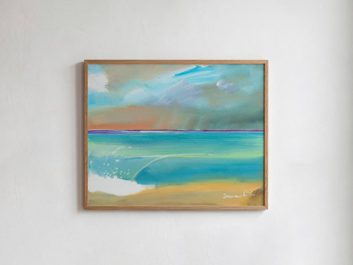 A framed landscape painting of a beach and ocean, featuring turquoise water, a sandy shore, and a cloudy sky, hung on a white wall.