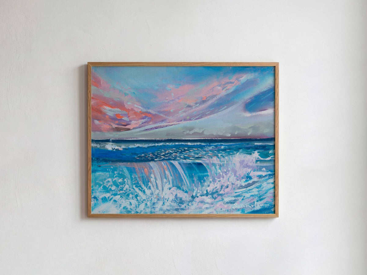 A framed painting of an ocean wave under a dramatic pink and blue sky, hung on a plain white wall.